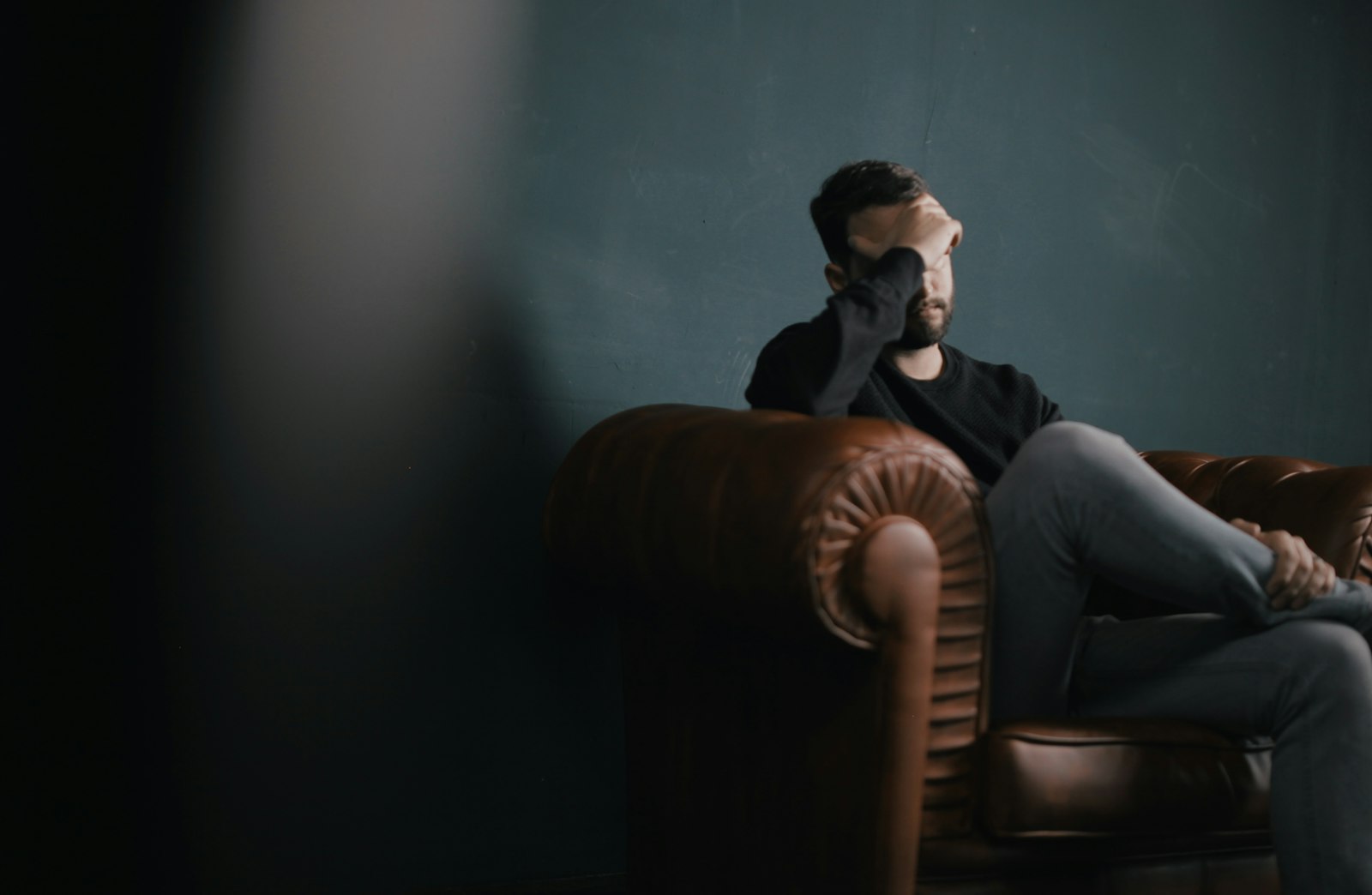 Un homme est assis sur un canapé, la tête entre les mains, inquiet à propos de la pression liée à se