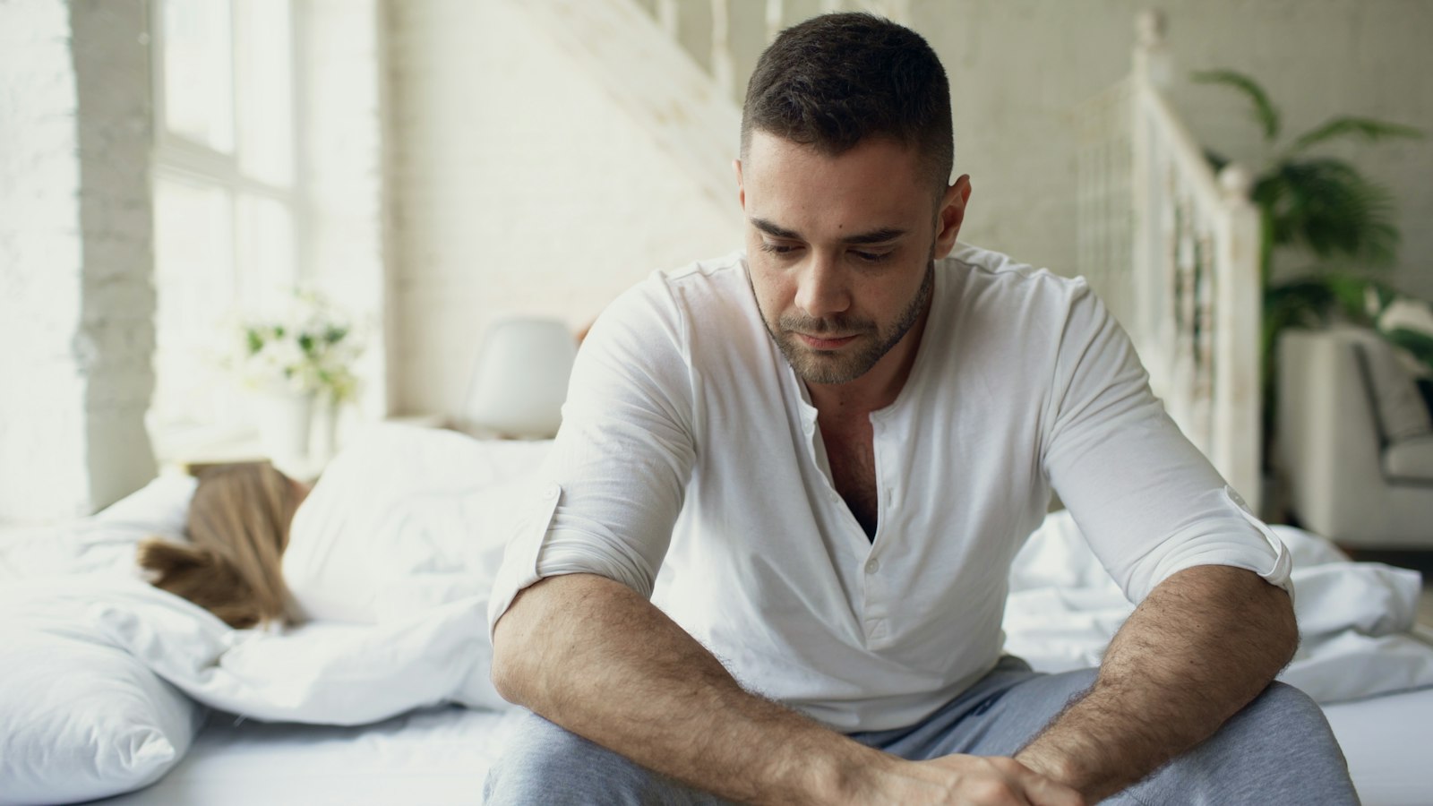 Man sitting on bed looking down thoughtfully